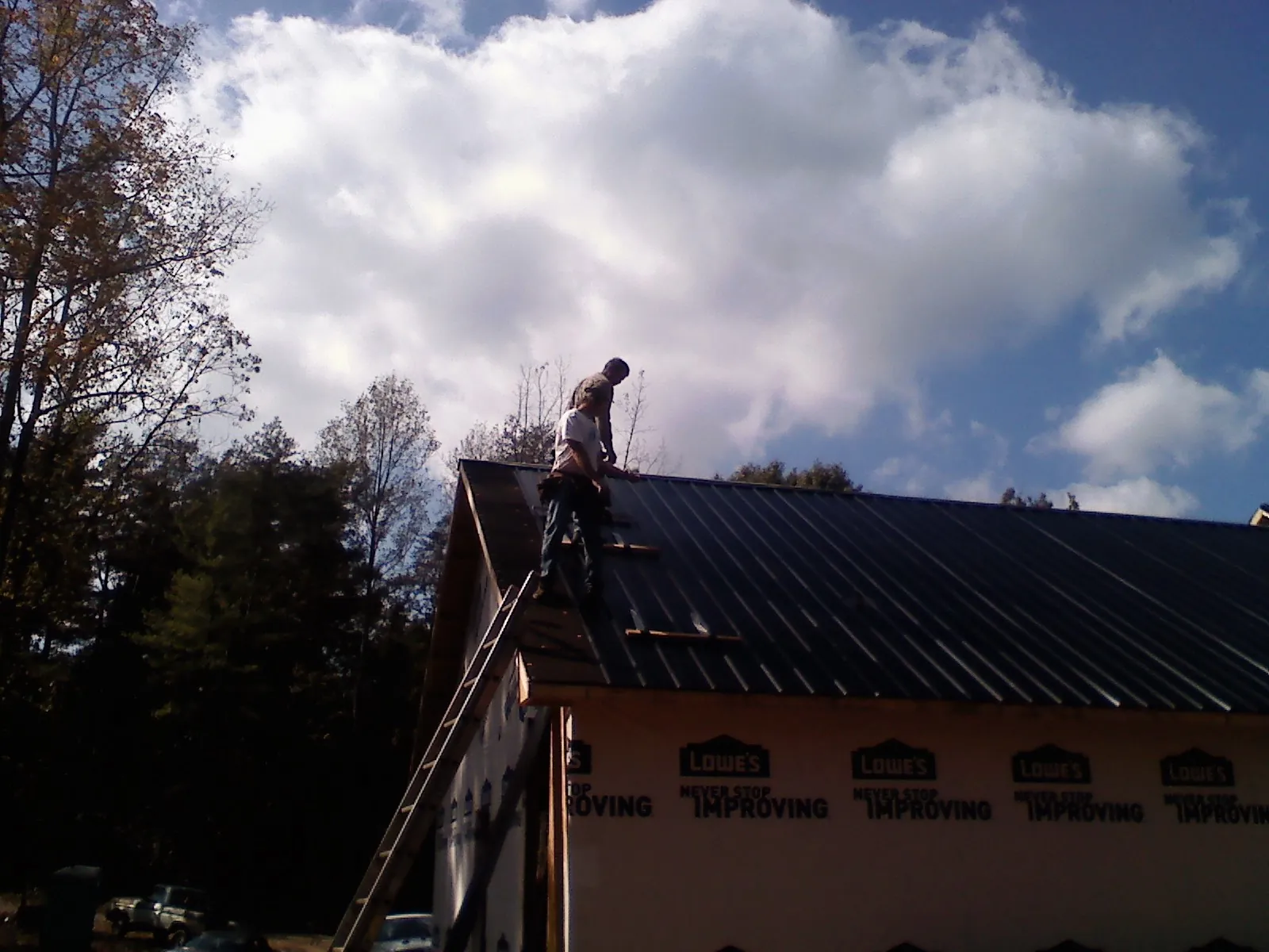 Roofer fastening dark metal panels high against a cloudy sky, from a Roof Inspection job in Pendleton